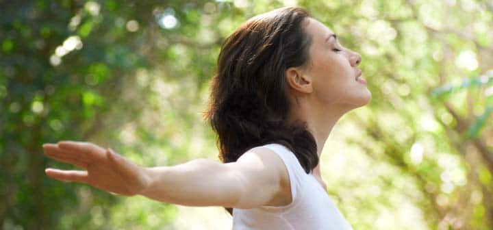 woman with her arms in the air on a sunny day breathing and optimistic